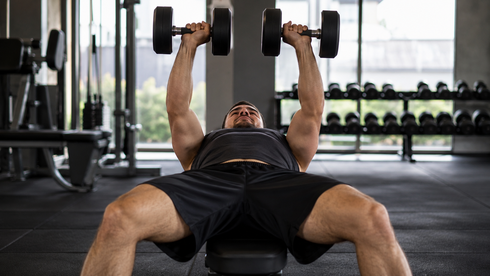 A lifter pressing dumbbells on a flat bench in a gym