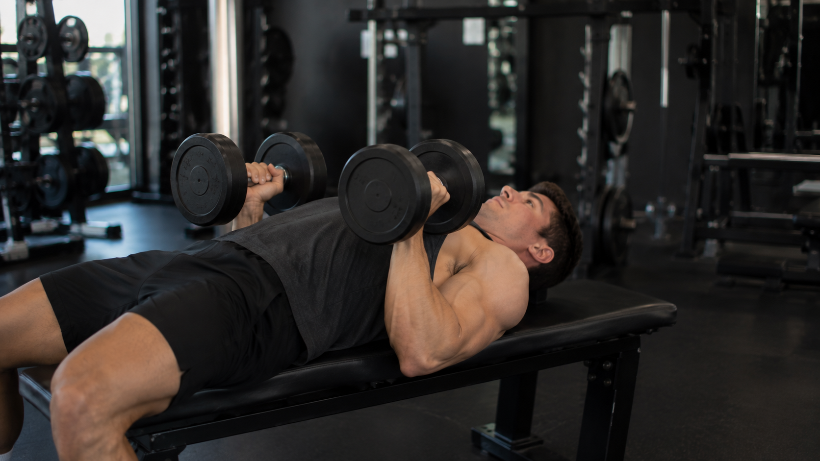 Lifter on a flat bench doing a dumbbell Tate press with elbows tucked